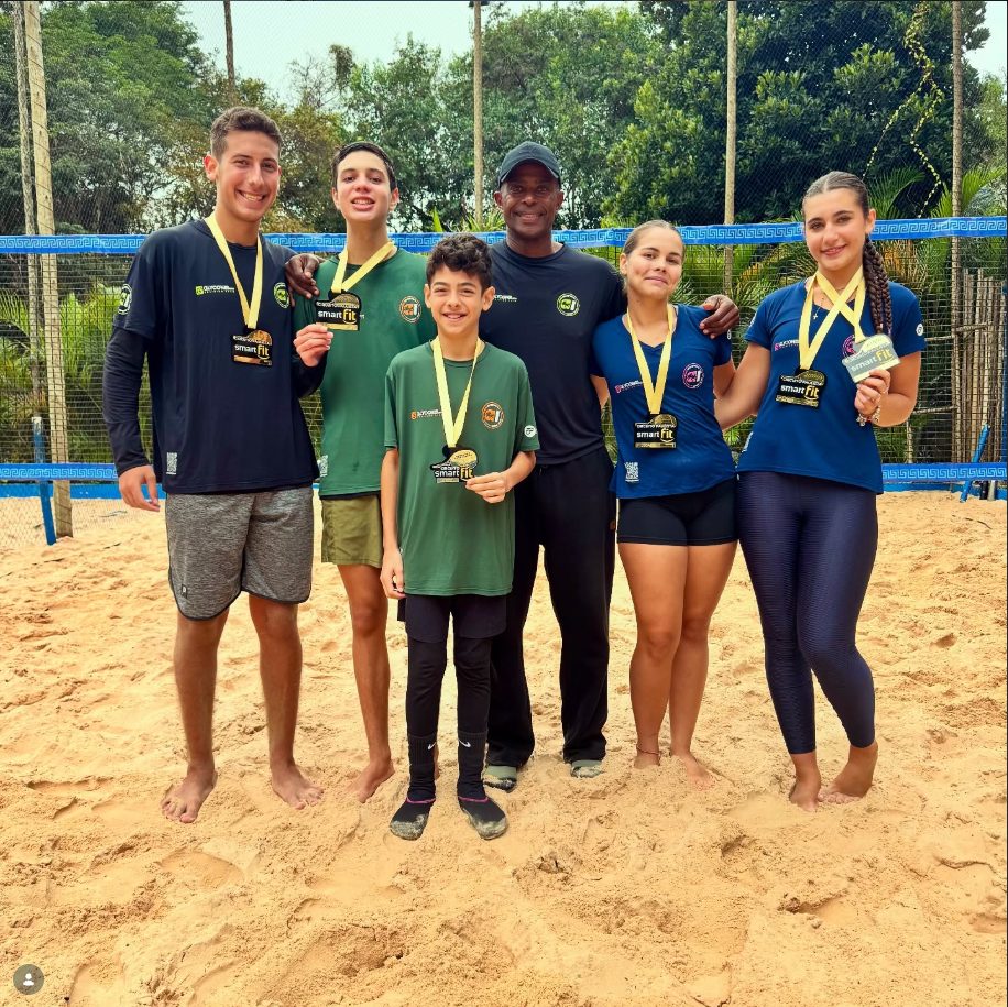 Grupo de atletas em quadra de areia com medalhas